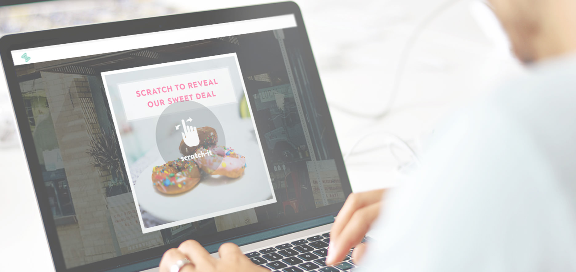 Person Using A Laptop Displaying An Image Of Donuts With Text &Quot;Scratch To Reveal Our Sweet Deal&Quot; And A Hand Cursor Indicating The Scratch Area.