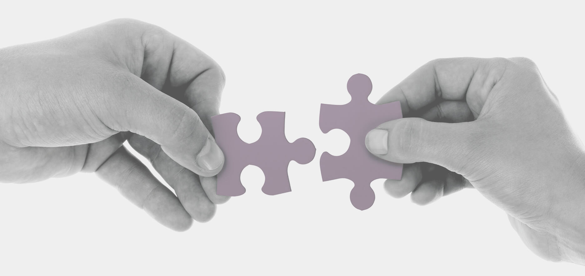 Two Hands Hold Purple Puzzle Pieces, Aligning Them To Fit Together On A Plain White Background.