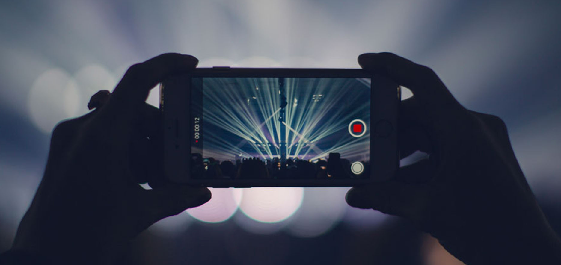 A Person Records A Concert With A Smartphone, Capturing Bright Stage Lights And A Crowd In The Background.